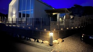 Een modern gebouw met een groot glazen raam, een houten terras en een metalen hek.
