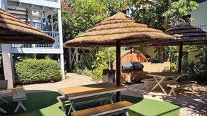 Un'area patio con ombrelloni di paglia, tavoli da picnic e un barbecue.