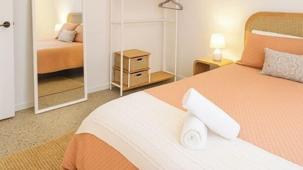 Una camera d'albergo con un letto, un armadio, uno specchio, un comodino con una lampada e un piccolo scrigno di legno.