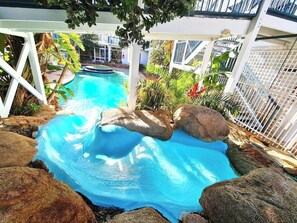 Una piscina con tobogán de agua, rodeada de rocas y plantas.