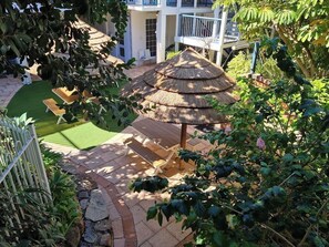 A thatched-roof gazebo surrounded by a garden with a lawn and a stone pathway. - Casa Coastal • Scarborough Beach • Ground Floor (Scarborough)