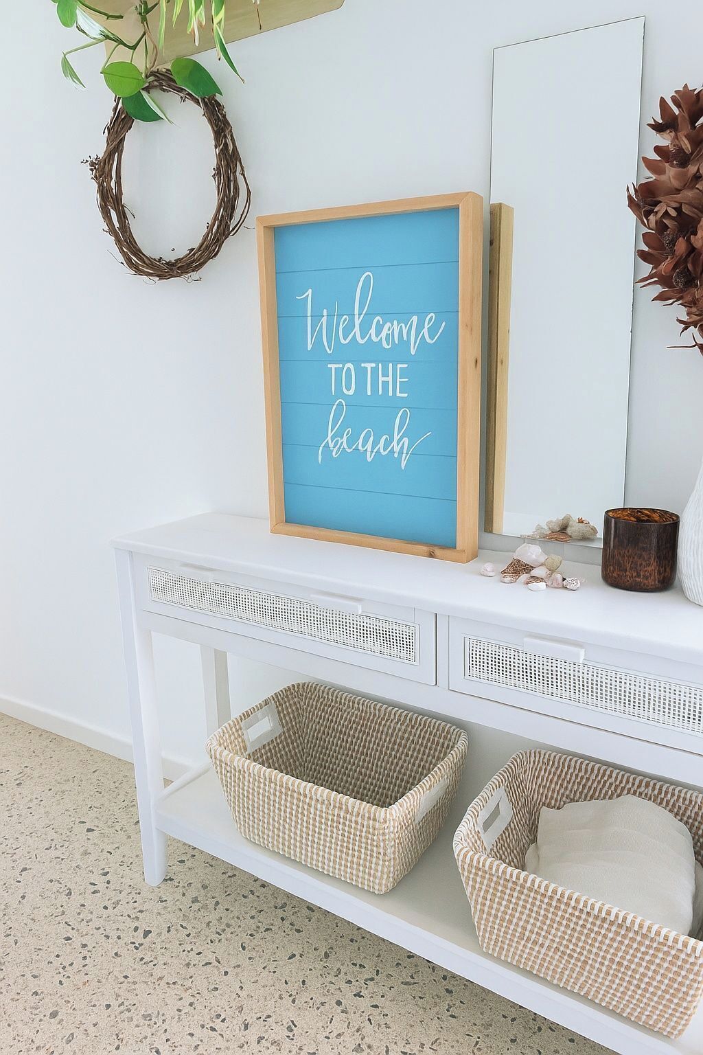 A white console table with a framed sign that reads 'Welcome to the beach.'