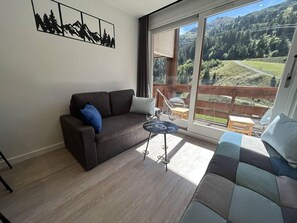Ein Wohnzimmer mit einer Couch, einem kleinen Tisch mit Weingläsern und einem Balkon mit Blick auf eine bewaldete Landschaft.