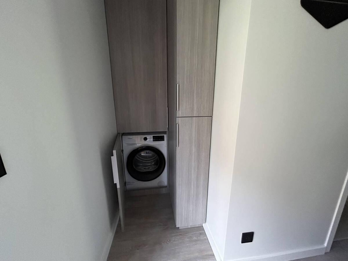 A laundry room with a washing machine and a dryer, wooden cabinets, and a white wall.