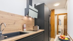 Cozinha moderna com painel de madeira, armários pretos e uma pia de aço inoxidável.