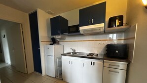Une cuisine de taille réduite avec des meubles blancs, une cuisinière et un four à micro-ondes.