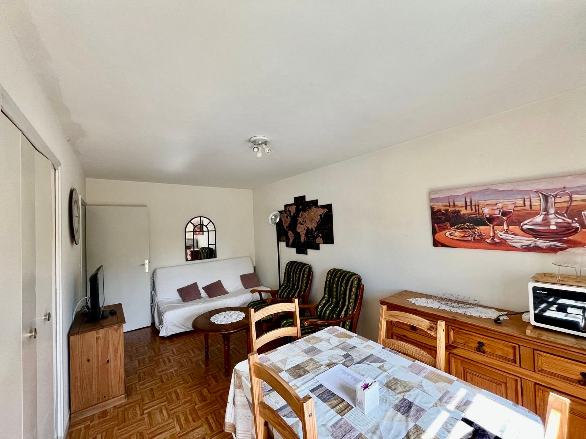 Um quarto aconchegante com cama, uma mesinha, uma cadeira, escrivaninha e televisão.