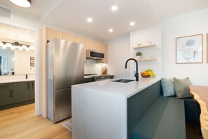 Une cuisine moderne dotée d’un îlot central intégré, d’appareils électroménagers en acier inoxydable et d’un coin salon avec des coussins.