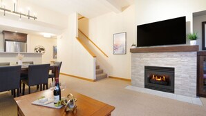 Ein modernes Wohnzimmer mit Kamin, Essbereich und einer Küche im Hintergrund.