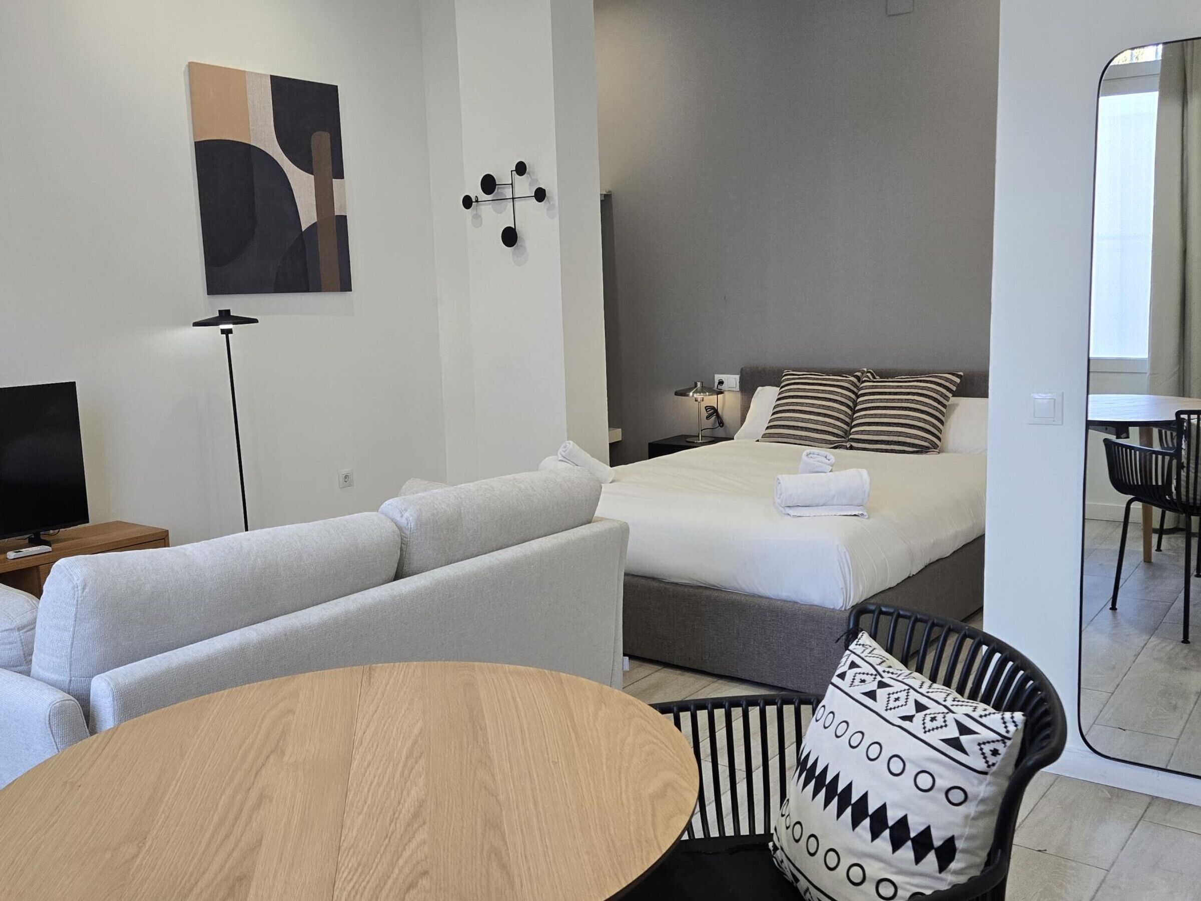 A modern hotel room with a bed, a sofa, a dining table, and a TV.