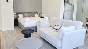 Ein modernes Schlafzimmer mit einem Bett, einem grauen Sofa, einem runden Tisch und einem Spiegel.