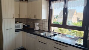 Eine Küche mit weißen Schränken, einer Mikrowelle, einer Kaffeemaschine und einem Fenster mit Spitzenvorhängen.