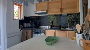 A kitchen with wooden cabinets, a stove, a microwave, and a window with curtains. - Charming house in Biscarrosse with terrace and parking (Biscarrosse Plage)