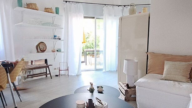 A modern living room with a round black table, a white sofa, and a dining area with a chair and table. - Charming house in Biscarrosse with terrace and parking (Biscarrosse Plage)