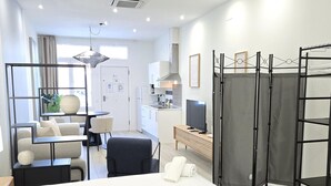 A modern hotel room with a bed, a desk, a chair, a TV, and a kitchenette in the background. - Designer Suites in Málaga, Authentic District (Málaga)