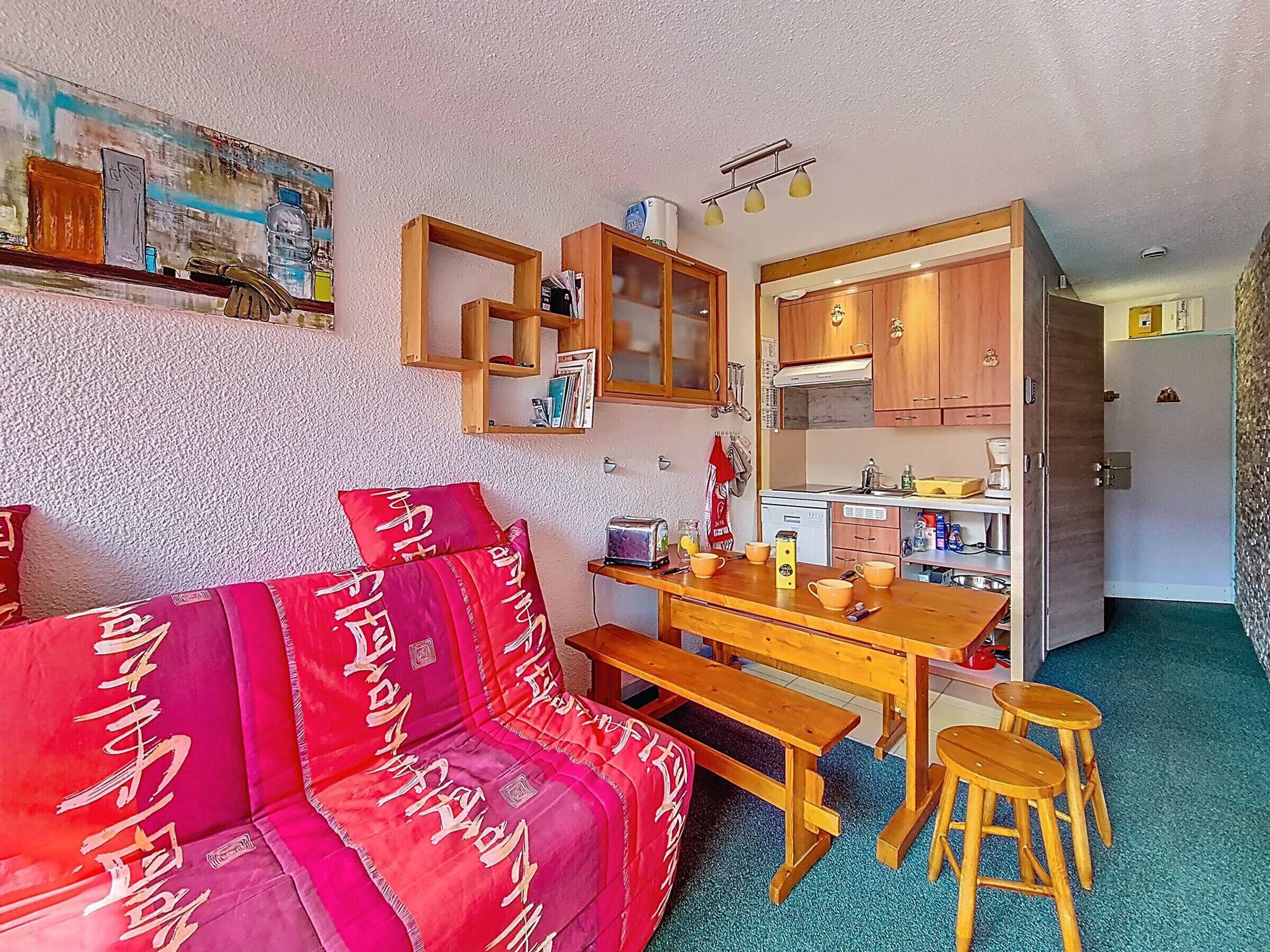 Un salon chaleureux avec un canapé rouge, une table basse en bois et un coin cuisine doté de meubles et d’un plan de travail en bois.
