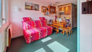 Un espacio habitable compacto con un sofá tapizado en rojo, una mesa de comedor de madera y una kitchenette con armarios y microondas.