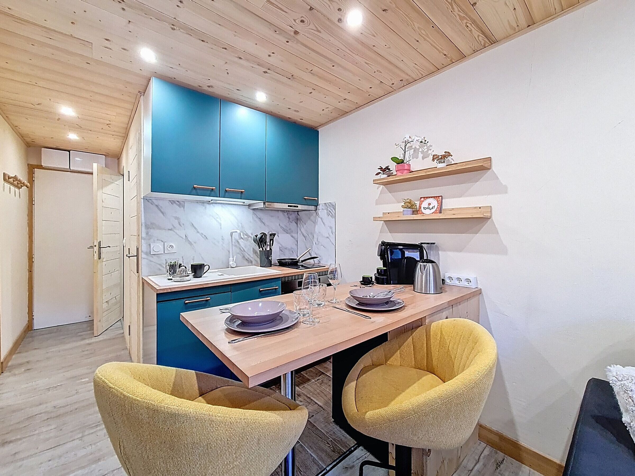 Una cucina compatta con mobili azzurri, un tavolo in legno e due sedie gialle.
