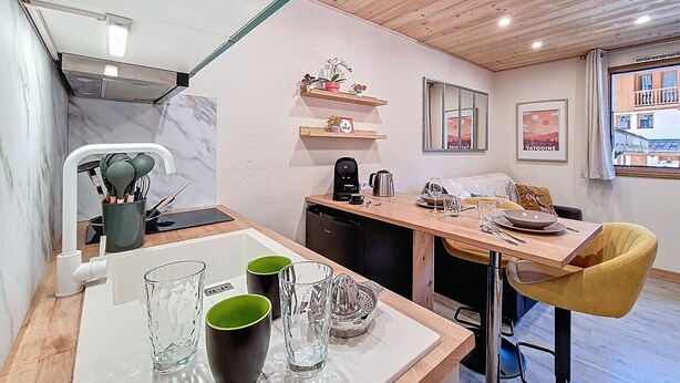 Cozinha moderna com bancada de madeira, cafeteira e área de refeições com uma cadeira amarela.