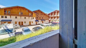 Fileira de edifícios de madeira com varandas, área de estacionamento com carros e um céu azul claro.