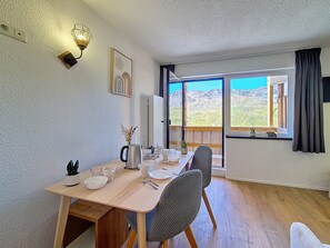 Ein Essbereich mit Tisch für vier Personen, Blick auf Berge durch große Fenster und einer modernen Wandleuchte.