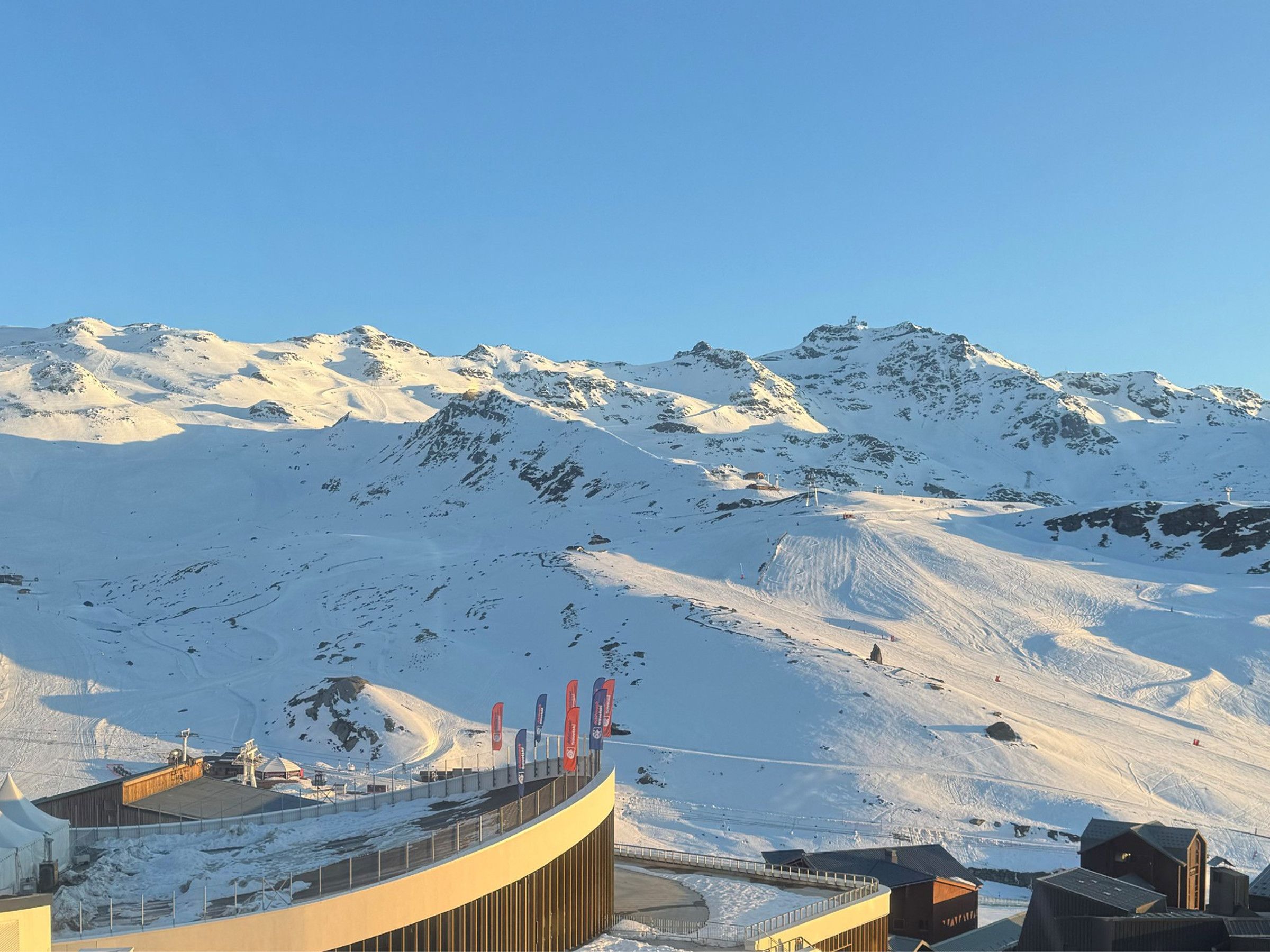 Eine verschneite Berglandschaft mit einem modernen Gebäude, das ein gewundes Dach und mehrere rote Fahnen aufweist.