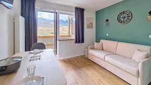 Ett rum med ett matbord, en soffa, utsikt över berg genom ett fönster och en väggklocka.