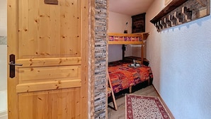 Een houten deur met een klein plaquette, een stapelbed met een kleurrijke deken, en een kamer met steenaccenten en een kamerbreed tapijt.