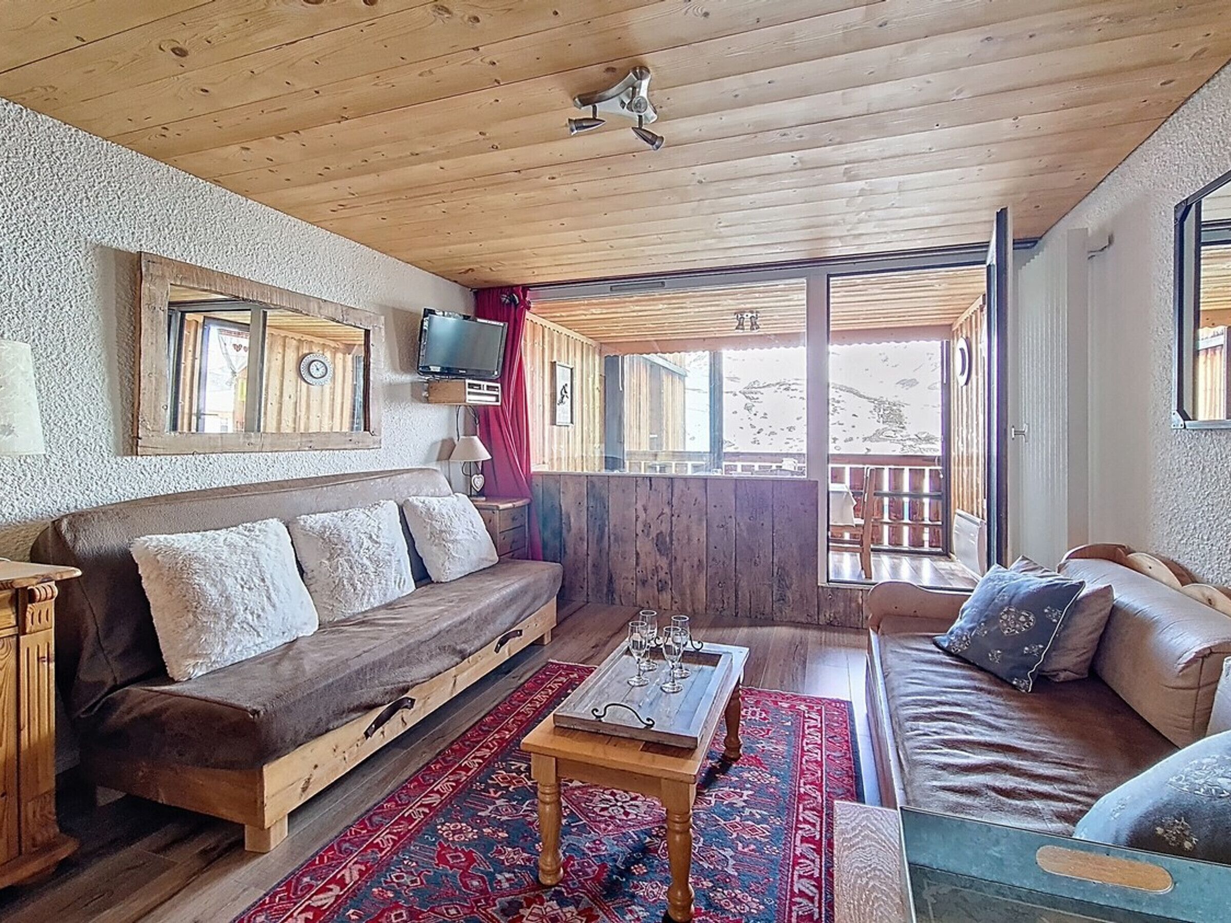 A cozy cabin interior with a wooden ceiling, a sofa, a coffee table, and a TV mounted on the wall.
