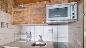 Een kleine keuken met houten kastjes, een magnetron, een spoelbak en een vaatwasser.