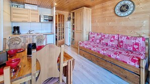 Interior acogedor de una cabaña con techo de madera, zona de comedor con mesa y sillas, kitchenette y un sofá con funda estampada.