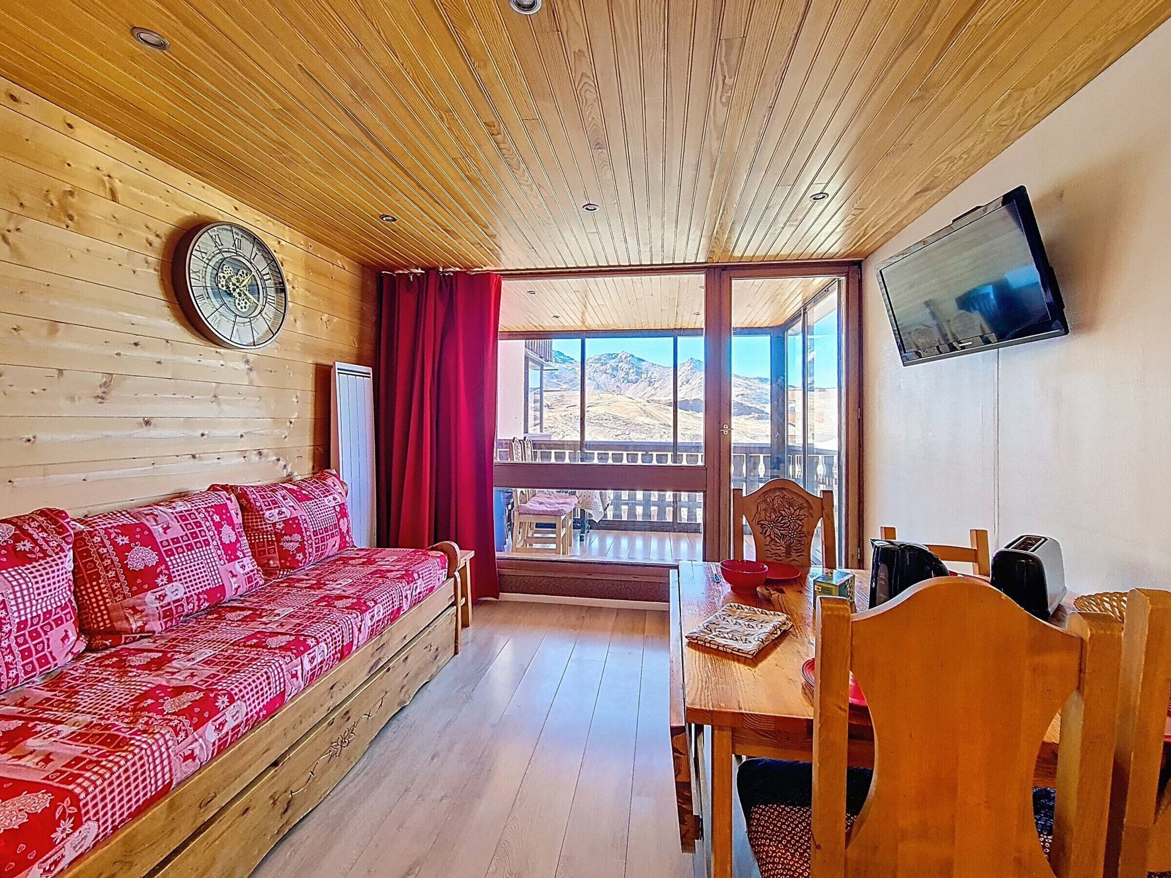 A wooden interior with a sofa, dining table, chairs, a TV, and a view of mountains.
