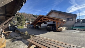 Un bâtiment en bois doté d’un espace de stationnement couvert, d’une table de pique-nique et d’une voiture garée à l’intérieur.