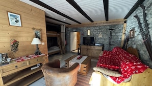 Une pièce chaleureuse avec un lit superposé en bois, un canapé rouge, un bureau en bois et un mur en pierre.