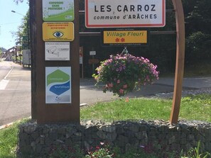 Ein Wegweiser mit mehreren Hinweisschildern, darunter eines für 'LES CARROZ commune d'ARACHES' und ein weiteres für 'Village Fleuri'.
