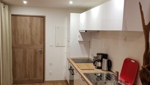 Een compacte keuken met houten vloeren, witte kasten, een roestvrijstalen spoelbak en een koffiezetapparaat.