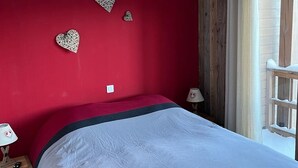 Een slaapkamer met een rode wand, een bed met een zwart-witte spreideken en decoratieve hartvormige wanddecoratie.