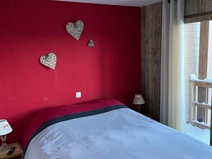 Ein Schlafzimmer mit roter Wand, einem Bett mit weiß-schwarzer Bettdecke und dekorativer Wandkunst in Herzform.