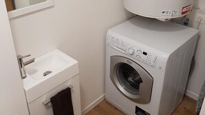 Een kleine wasruimte met een wasmachine, een wasbak en een spiegel.