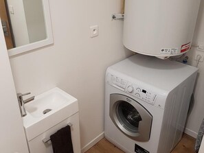 Ein kleiner Waschbereich mit Waschmaschine, Spüle und Spiegel.