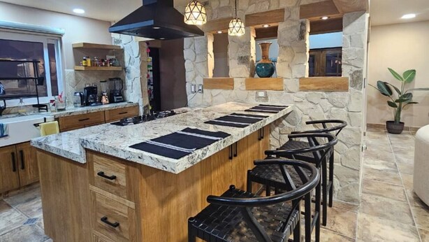 A modern kitchen with a central island, bar stools, a stone accent wall, and pendant lighting. - Flor del Desierto - Lovely house with cool AC in vibrant LORETO, BCS (BCS)