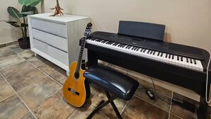 A music room with a piano, a guitar, a bench, a plant, and a framed picture on the wall. - Flor del Desierto - Lovely house with cool AC in vibrant LORETO, BCS (BCS)