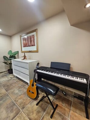 A music room with a piano, a guitar, a bench, a plant, and a framed picture on the wall. - Flor del Desierto - Lovely house with cool AC in vibrant LORETO, BCS (BCS)