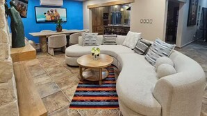 A modern living room with a large L-shaped sectional sofa, a coffee table, and a TV mounted on the wall. - Flor del Desierto - Lovely house with cool AC in vibrant LORETO, BCS (BCS)
