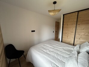 A bedroom with a bed, a chair, a wardrobe, and a light fixture. - New! Luxury 3-bedroom apartment with balcony and covered parking (Arâches-la-Frasse)