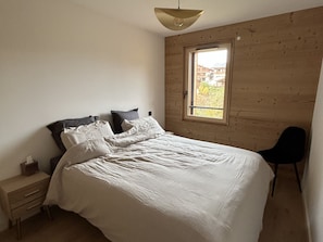 A bedroom with a bed, a nightstand, a chair, and a window. - New! Luxury 3-bedroom apartment with balcony and covered parking (Arâches-la-Frasse)
