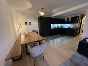 A modern kitchen with dark cabinetry and a dining area with a wooden table and chairs. - New! Luxury 3-bedroom apartment with balcony and covered parking (Arâches-la-Frasse)