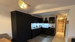 Uma cozinha moderna com armários escuros, uma mesa de jantar de madeira e uma luminária sobre o balcão.
