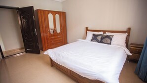 A bedroom with a wooden bed, white bedding, a wooden wardrobe, and a mirror. - Luxurious Three Bedroom House at Trassaco East Legon (Madina)