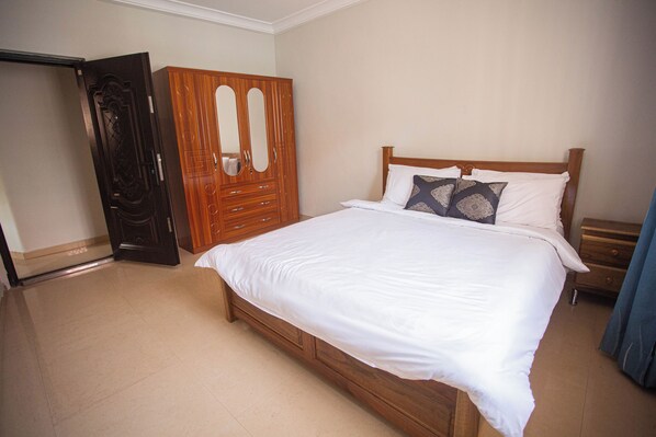 Un dormitorio con una cama de madera, ropa de cama blanca, un armario de madera y un espejo.